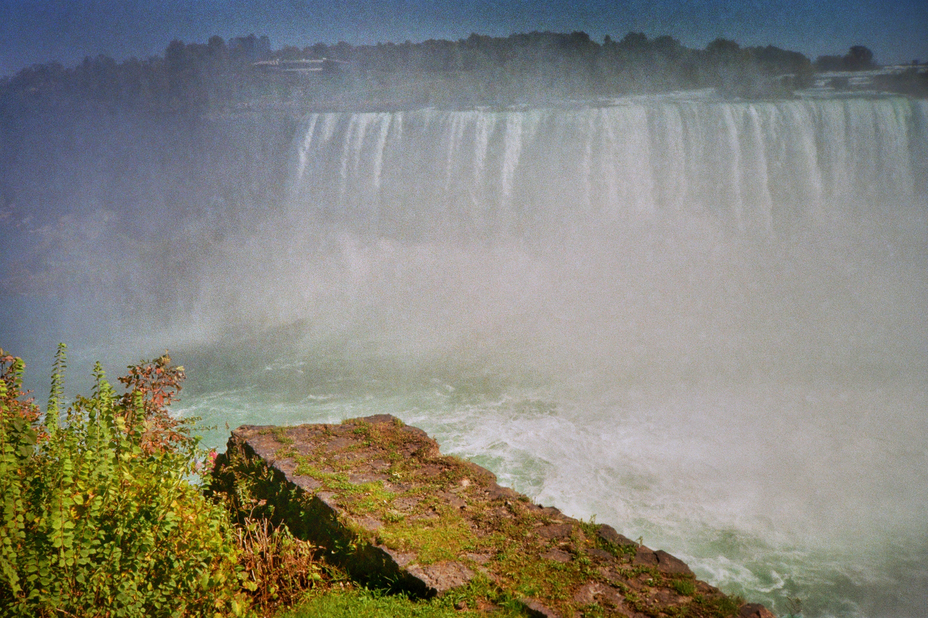 a picture of niagara falls, grainy and with muted colors, with them sort of fading into the background and a ledge in the foreground with bright green colors