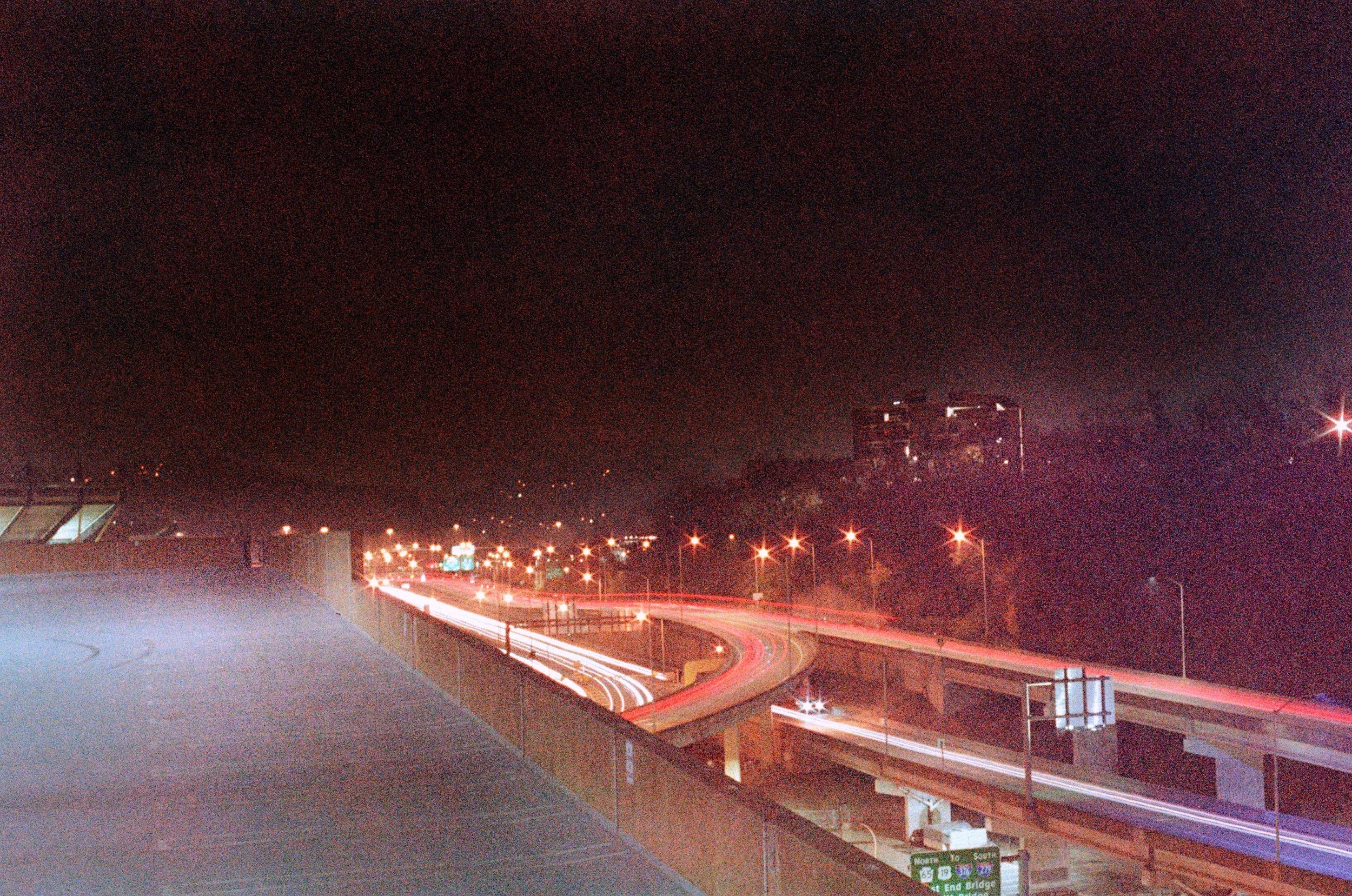 super grainy and distorted color photo of a highway overpass in northside pittsburgh. light trails. kind of eerie. from the top of a garage