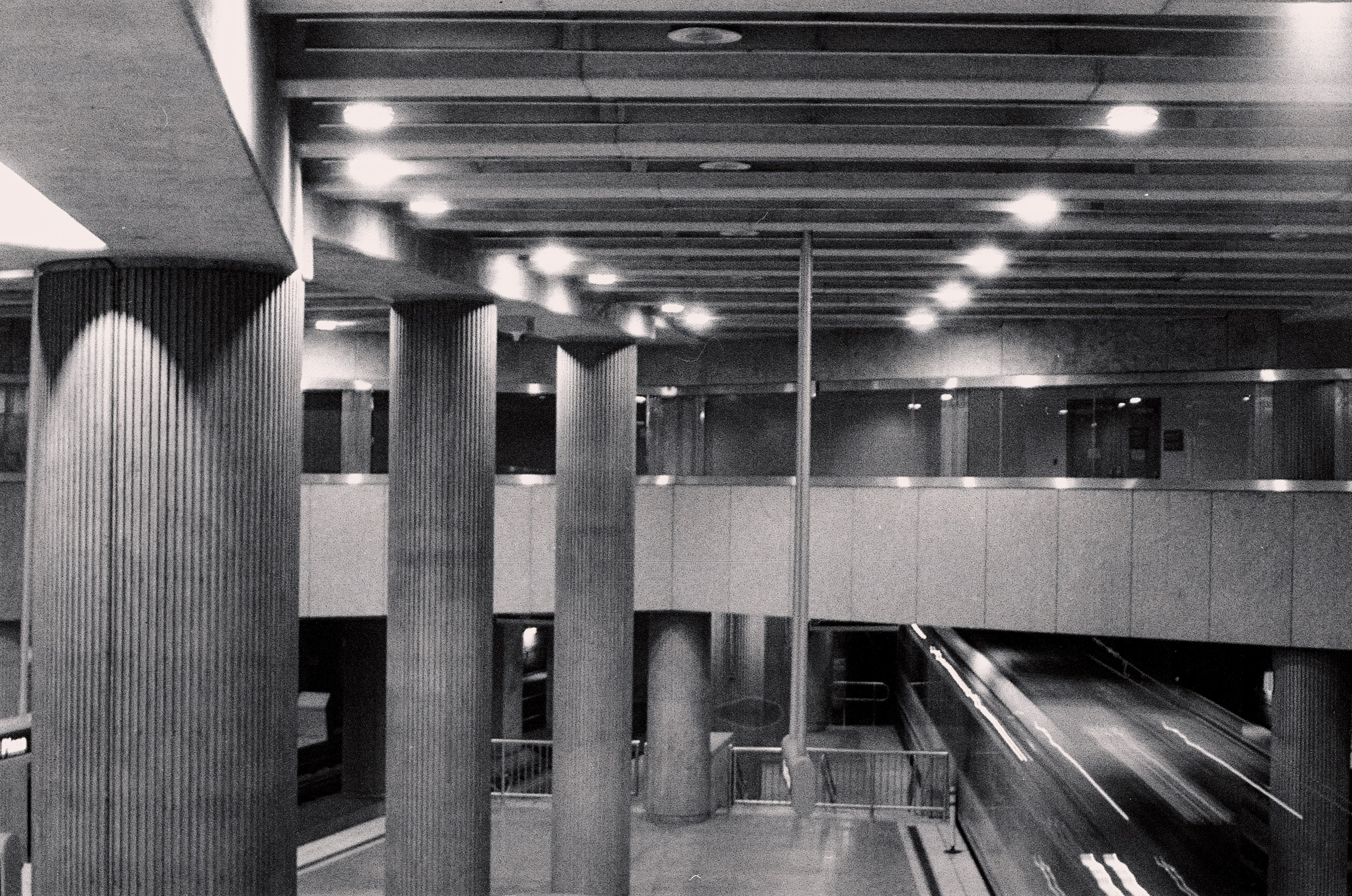 picture of a train tunnel, steel plaza in pittsburgh, black and white. lots of, like, geometrical things going on. train is blurring in the right of the frame.