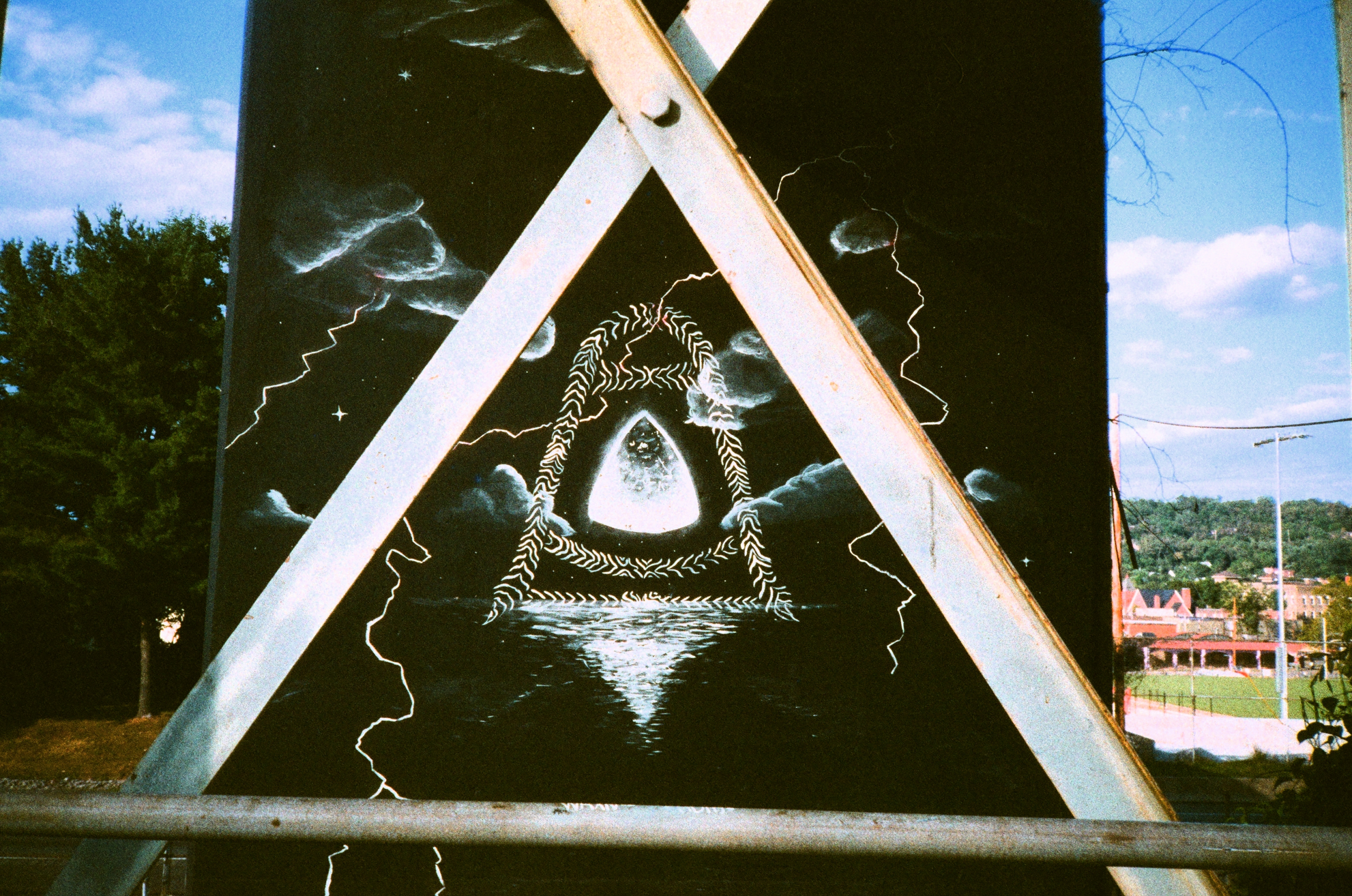 picture of a strange piece of graffiti between an X of metal depicting some sort of otherworldly portal reflecting over a lake